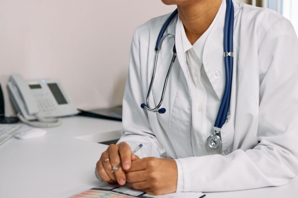 Doctor with stethoscope and white coat seated at a clinic desk.